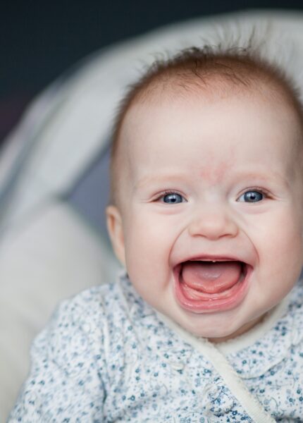 Portrait of adorable smiling baby infant showing first teeth.